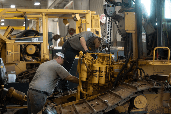 The image shows two technicians performing heavy machinery maintenance, a critical part of the industrial equipment lifecycle.